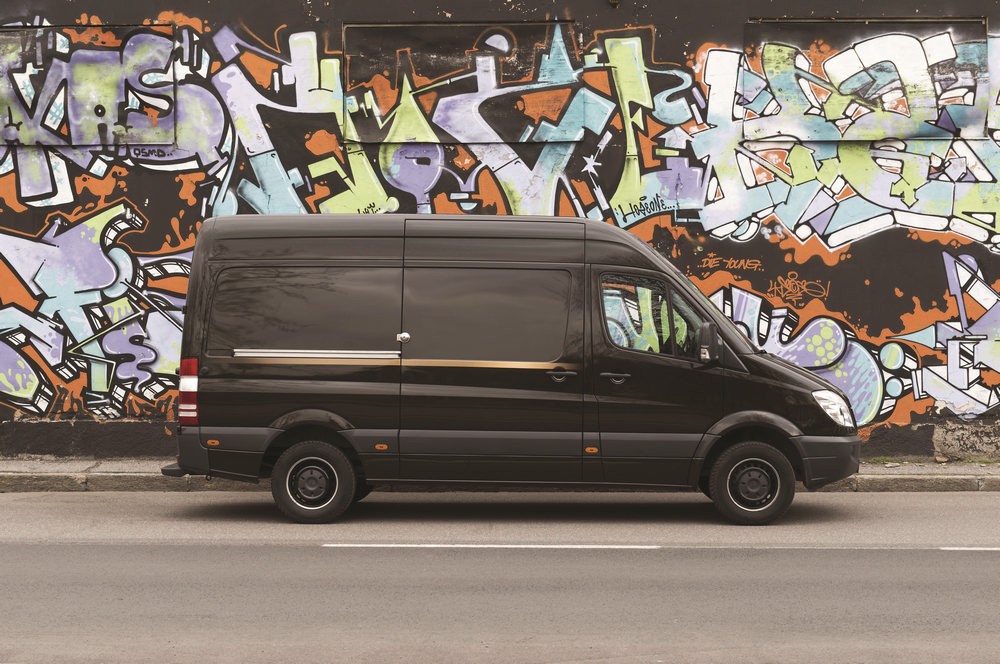 Furgone nero con lucchetto di sicurezza UFO Meroni modello UFO+ parcheggiato davanti a un muro con graffiti colorati.